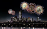 Nighttime cityscape lit by colorful fireworks bursting in the sky above.