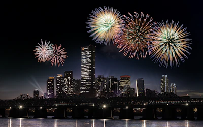 Nighttime cityscape lit by colorful fireworks bursting in the sky above.