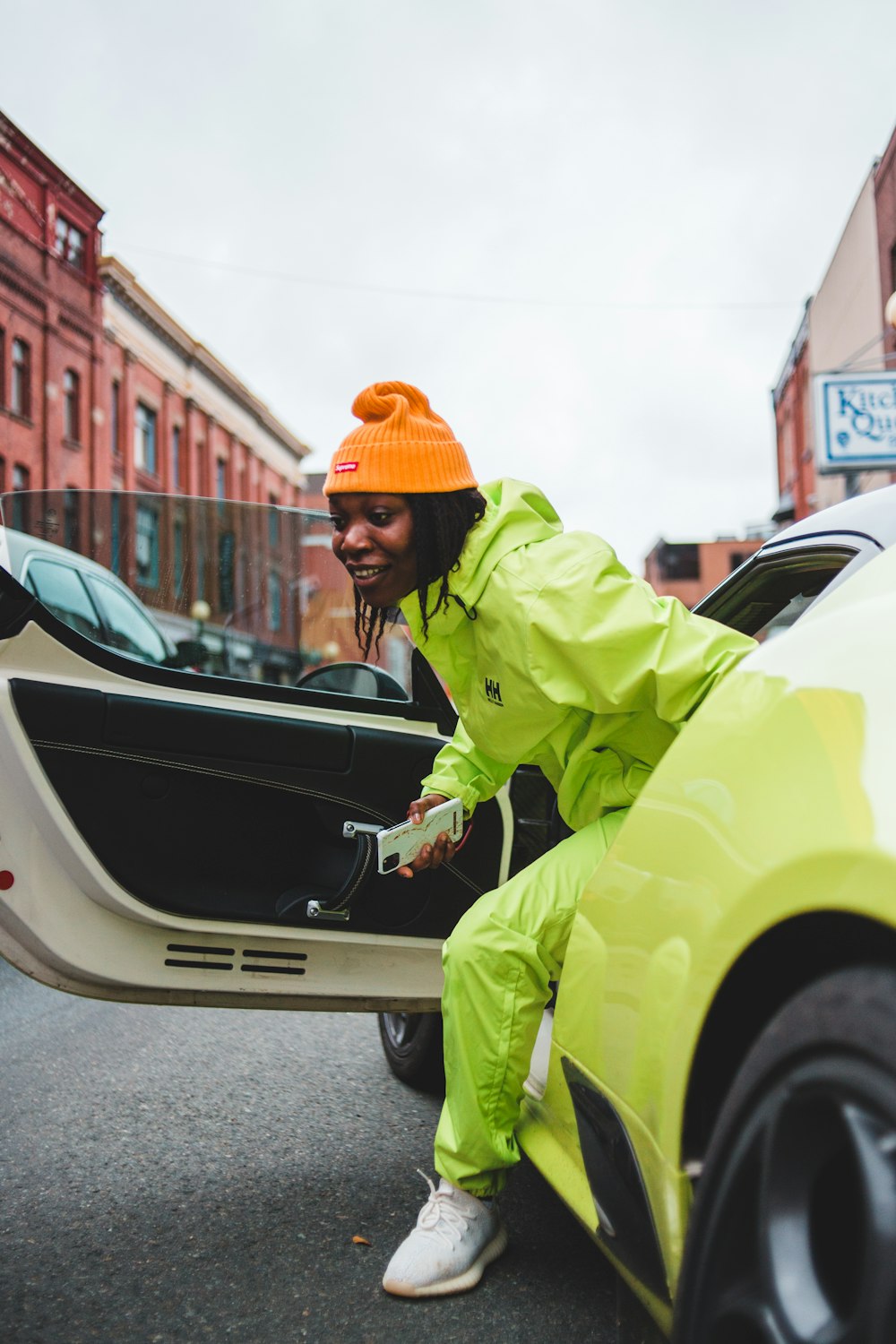 man in green jacket and orange knit cap standing beside black car during daytime