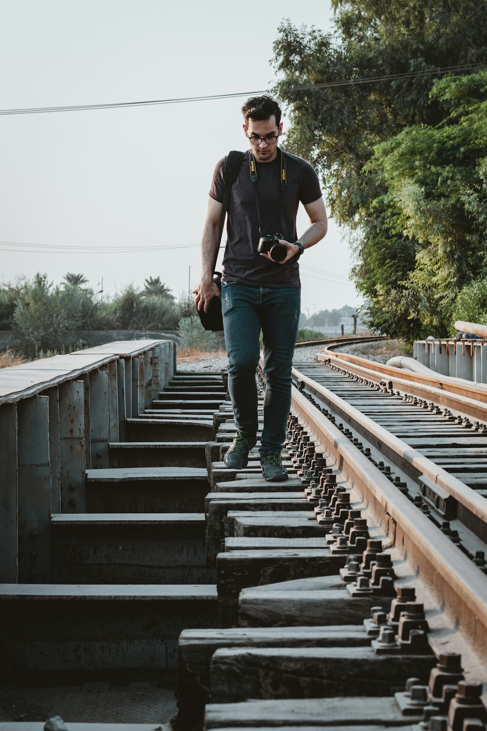 man in black crew neck t-shirt and blue denim jeans standing on brown wooden bridge