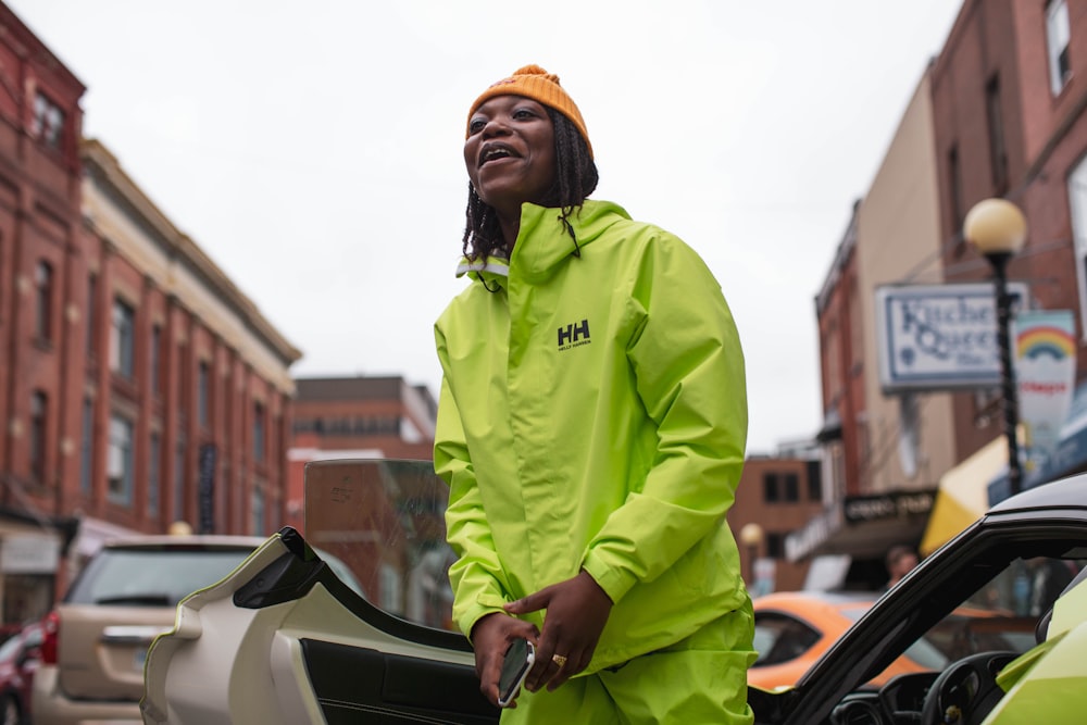 man in green hoodie standing beside black car during daytime