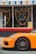 An orange sports car is parked in front of a shop. The shop has large windows with a sign displaying the words 'UNDER GROUND SNAX' in colorful letters inside shield-like outlines. Above the windows, a canopy with multicolored decorative shapes is visible. A yellow sign with 'BLACK LIVES MATTER' is placed near the entrance.