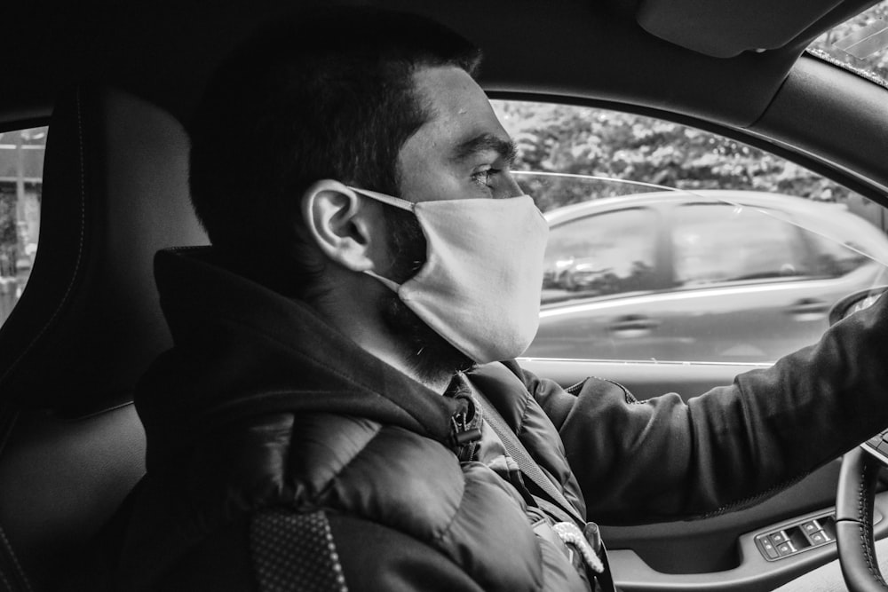 grayscale photo of man in jacket driving car