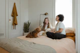 woman in white long sleeve shirt sitting on bed beside brown dog