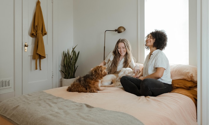 woman in white long sleeve shirt sitting on bed beside brown dog