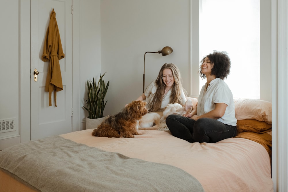 茶色の犬のそばのベッドに座っている白い長袖シャツの女性