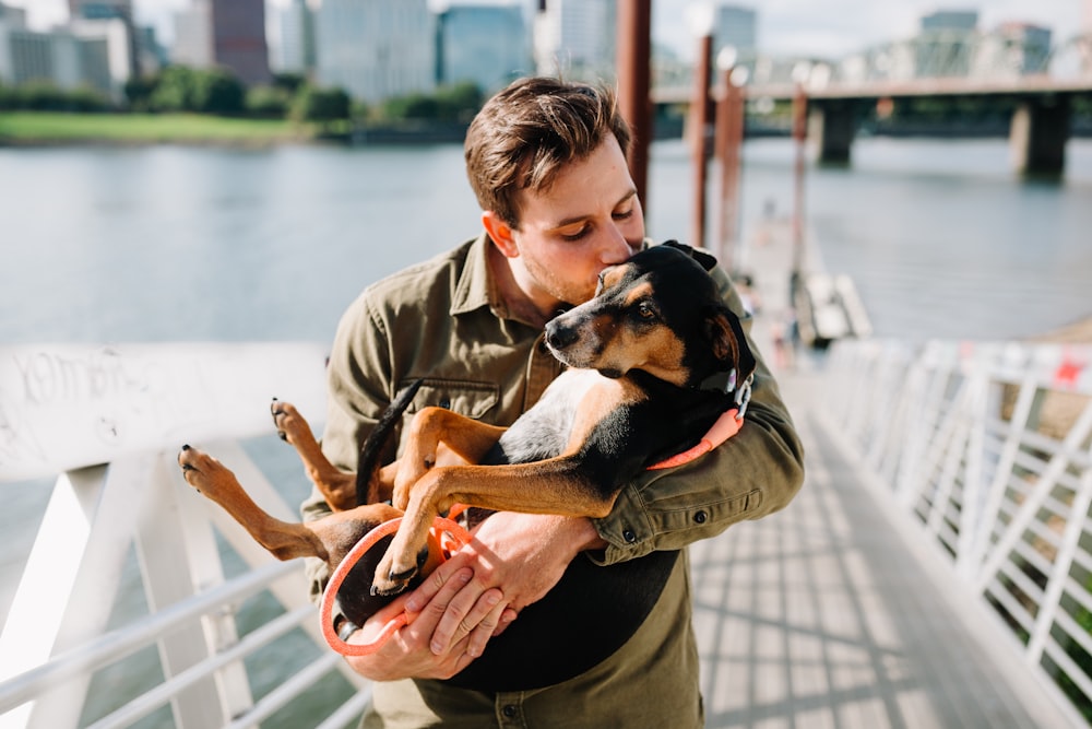 man in brown jacket hugging black and brown short coated dog