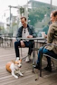 Cozy corner of the café with hanging ferns and warm light, showing a happy customer enjoying coffee with their dog.