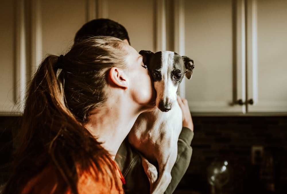 woman in orange shirt hugging white and black short coated dog