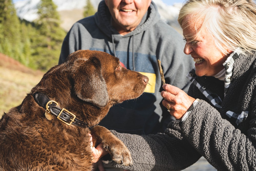 man in black jacket holding brown short coated dog