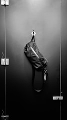 A rugged leather messenger bag hanging on a rustic hook against a textured wall.