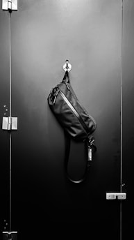 A rugged leather messenger bag hanging on a rustic hook against a textured wall.