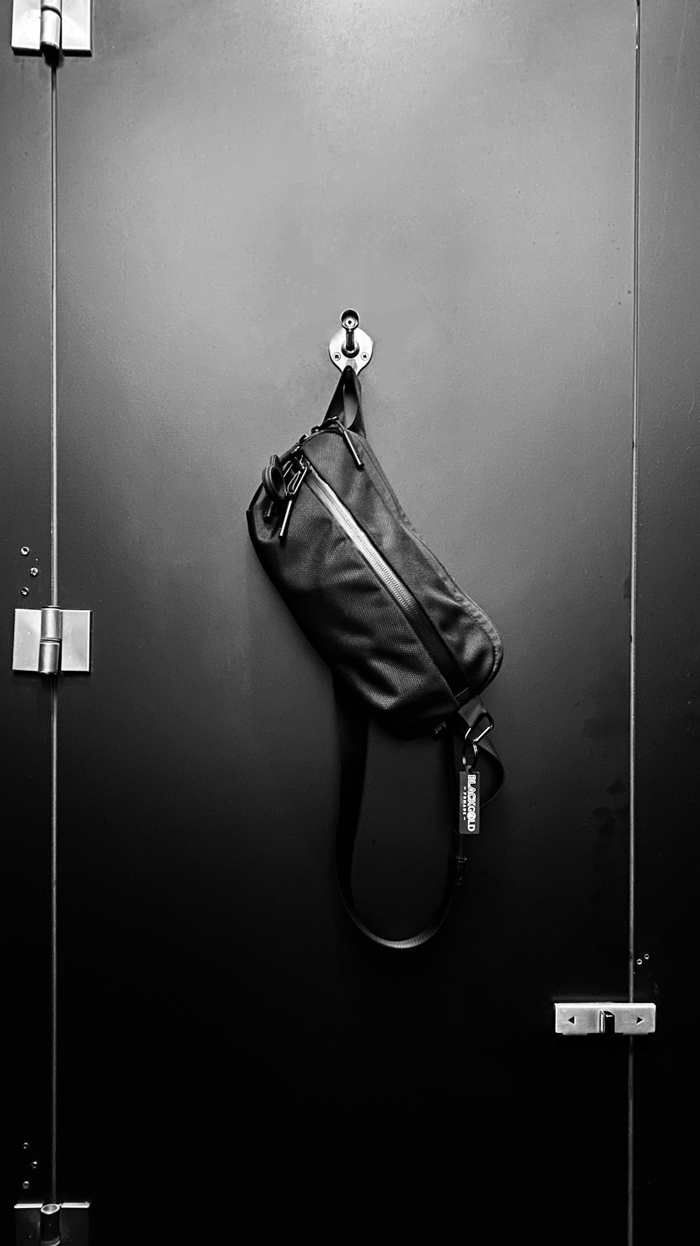 black leather sling bag hanging on door