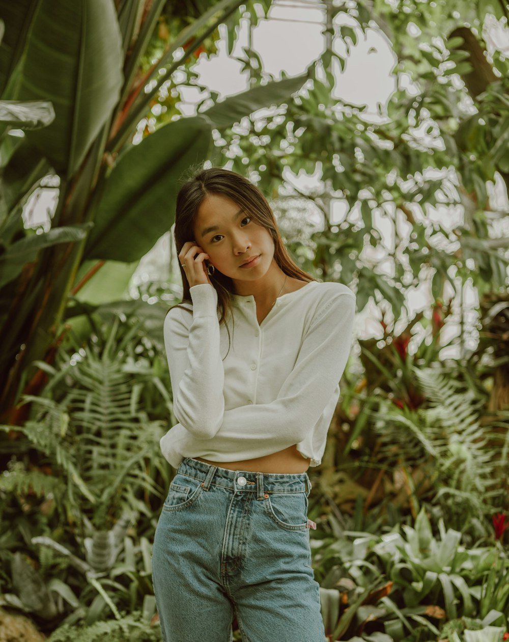 woman in white dress shirt and blue denim jeans standing near green plants during daytime