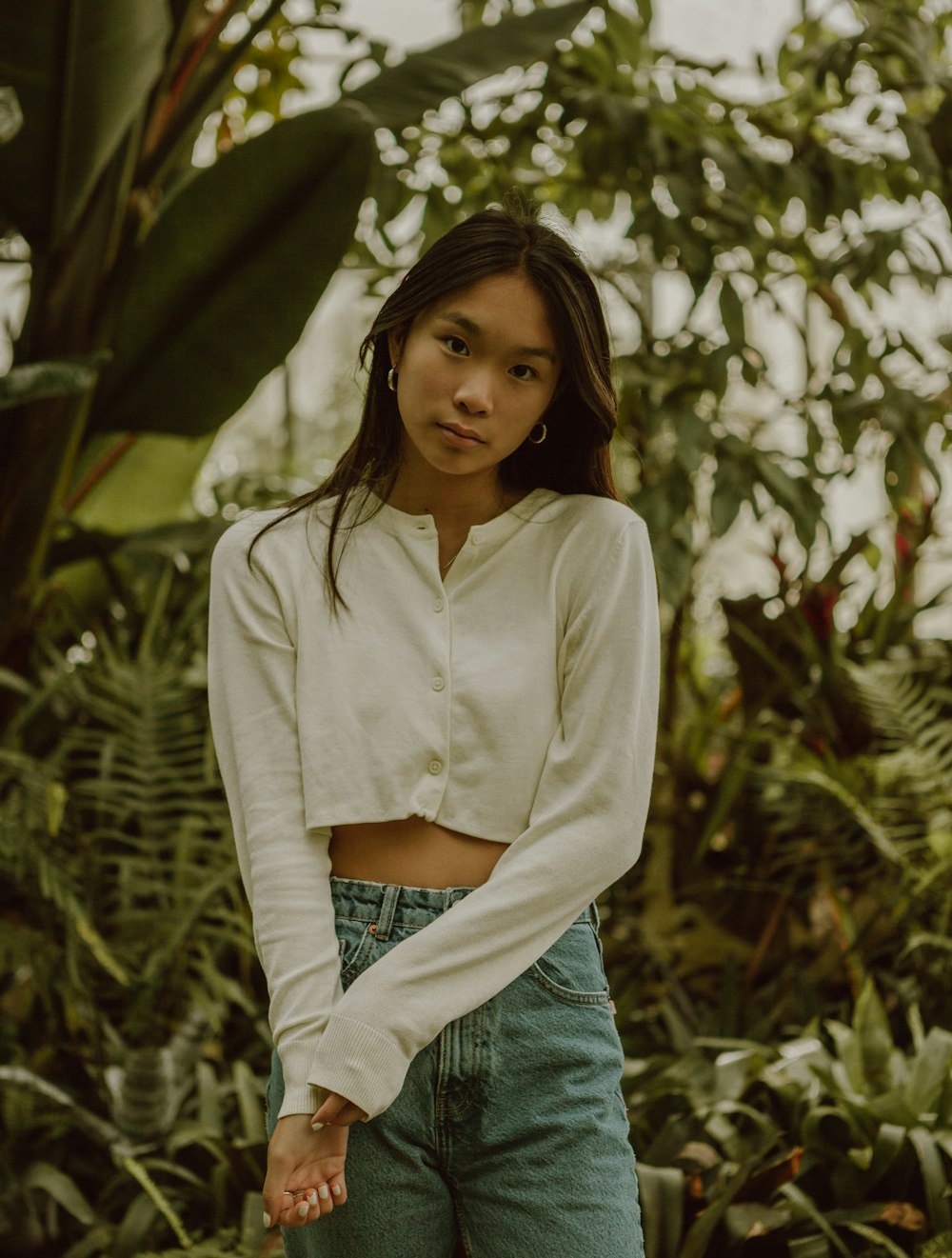 woman in white dress shirt and blue denim jeans standing near green plant during daytime