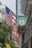 A large building facade featuring a green ornamental clock is adorned with multiple American flags. In the background, a prominent red and yellow sign spells out 'Chicago.' Trees and modern high-rise buildings are visible, highlighting an urban setting.