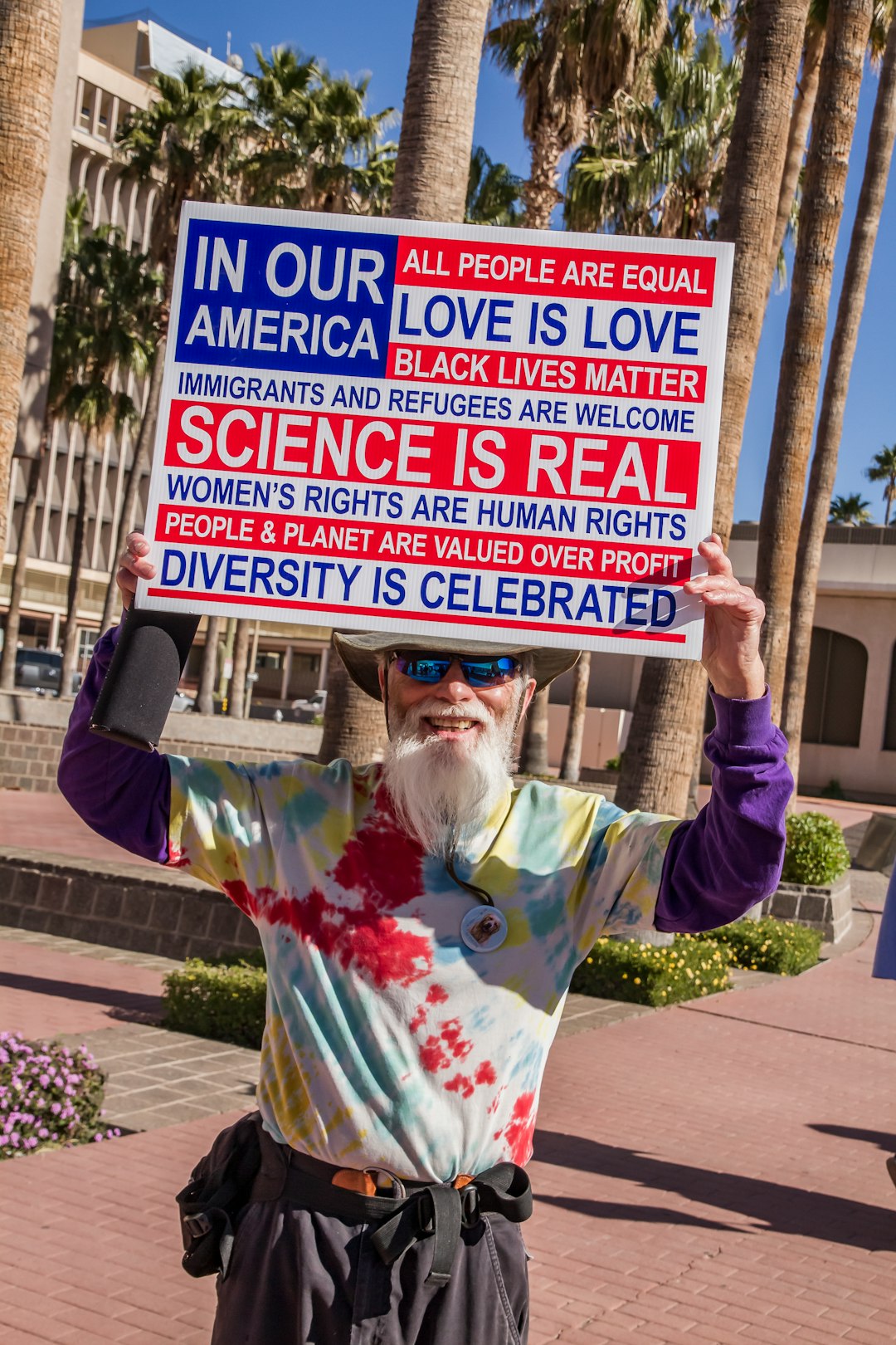 woman in white and pink floral long sleeve shirt holding blue and white signage