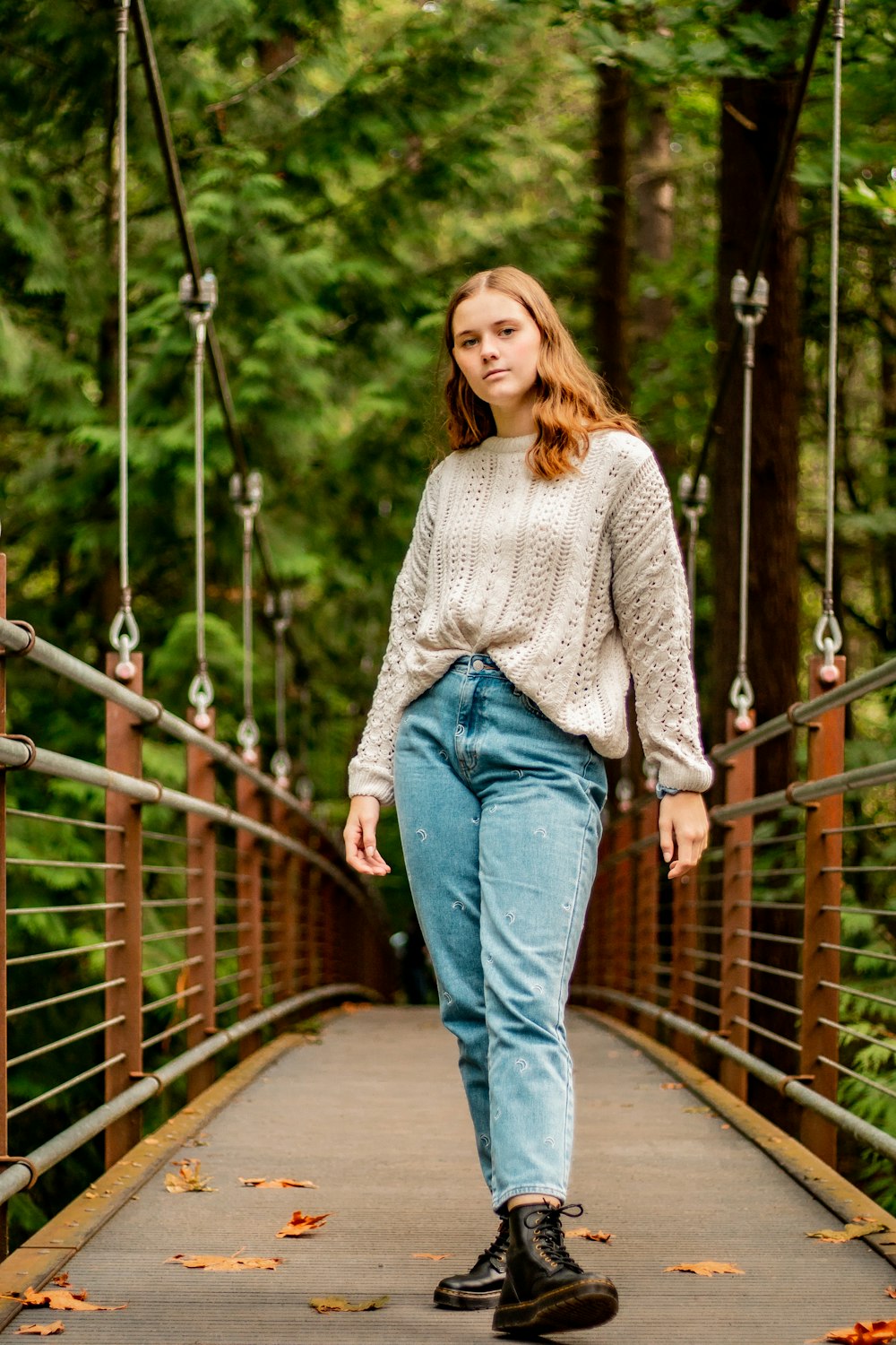 woman in gray sweater and blue denim jeans standing on bridge