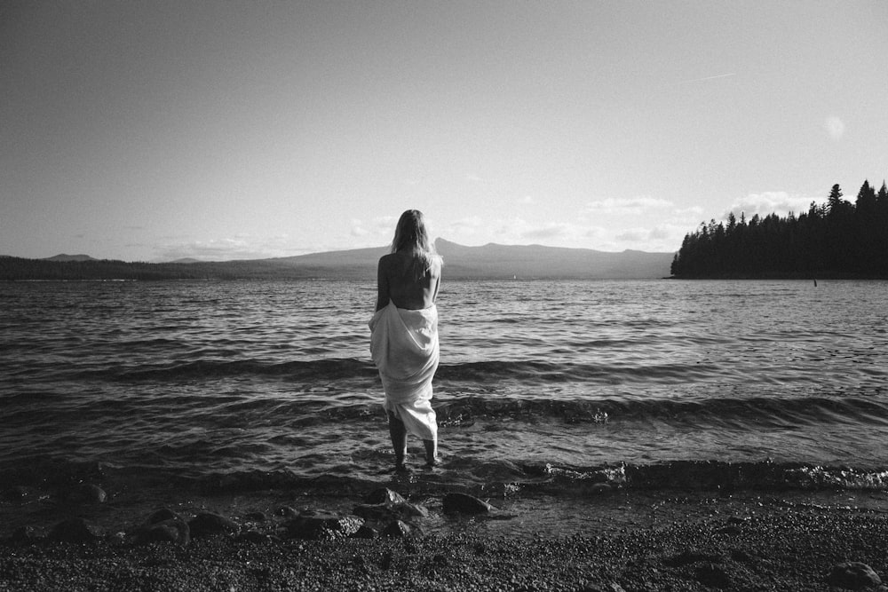 Mujer con camisa blanca de manga larga de pie en la orilla del mar