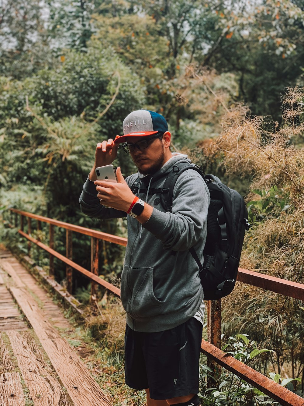 man in black jacket and gray cap holding red and black camera standing on brown wooden