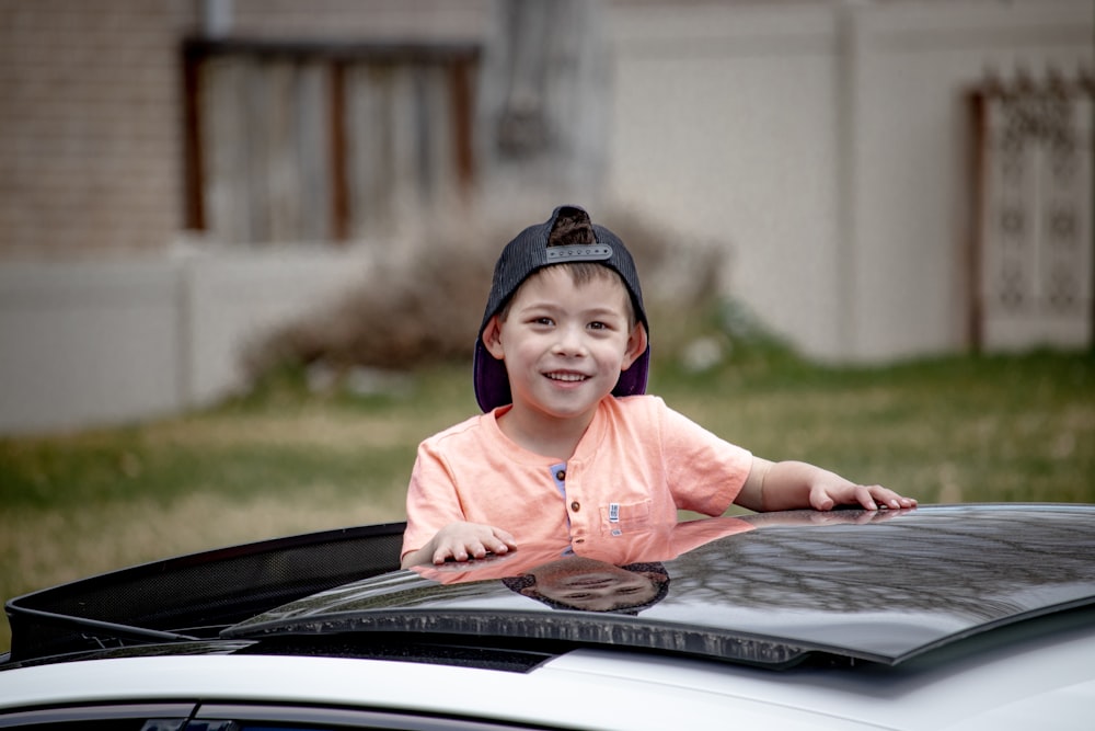 girl in pink long sleeve shirt and black knit cap sitting on black car hood during