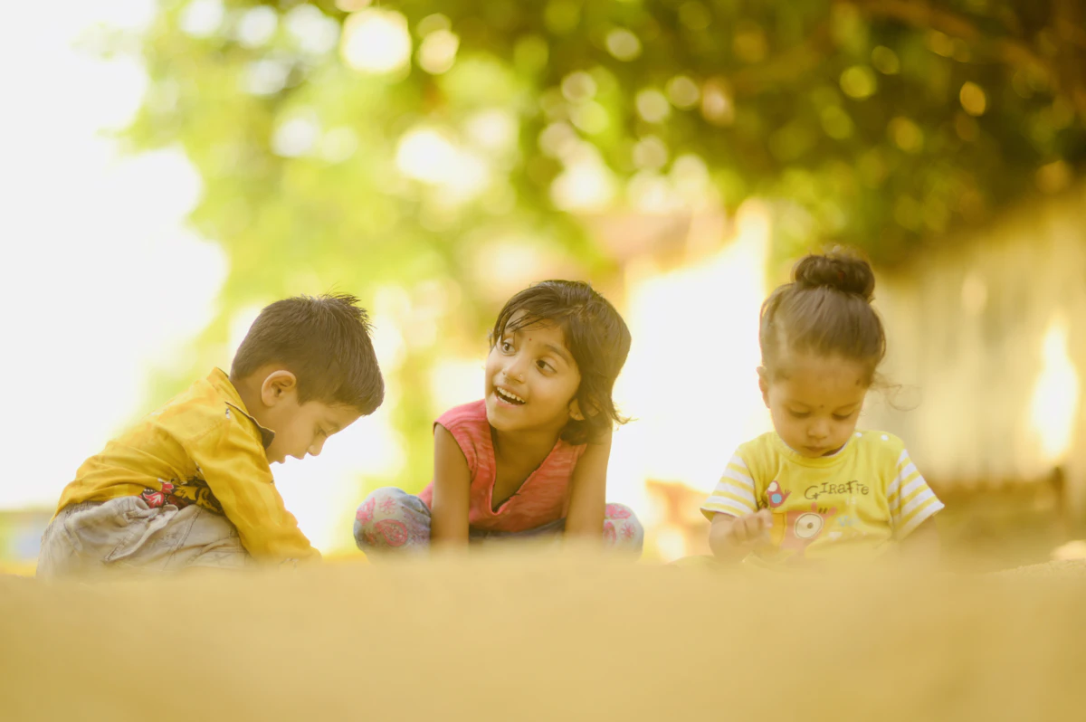 Three children joyfully playing with water guns on a sandy beach under the sun.