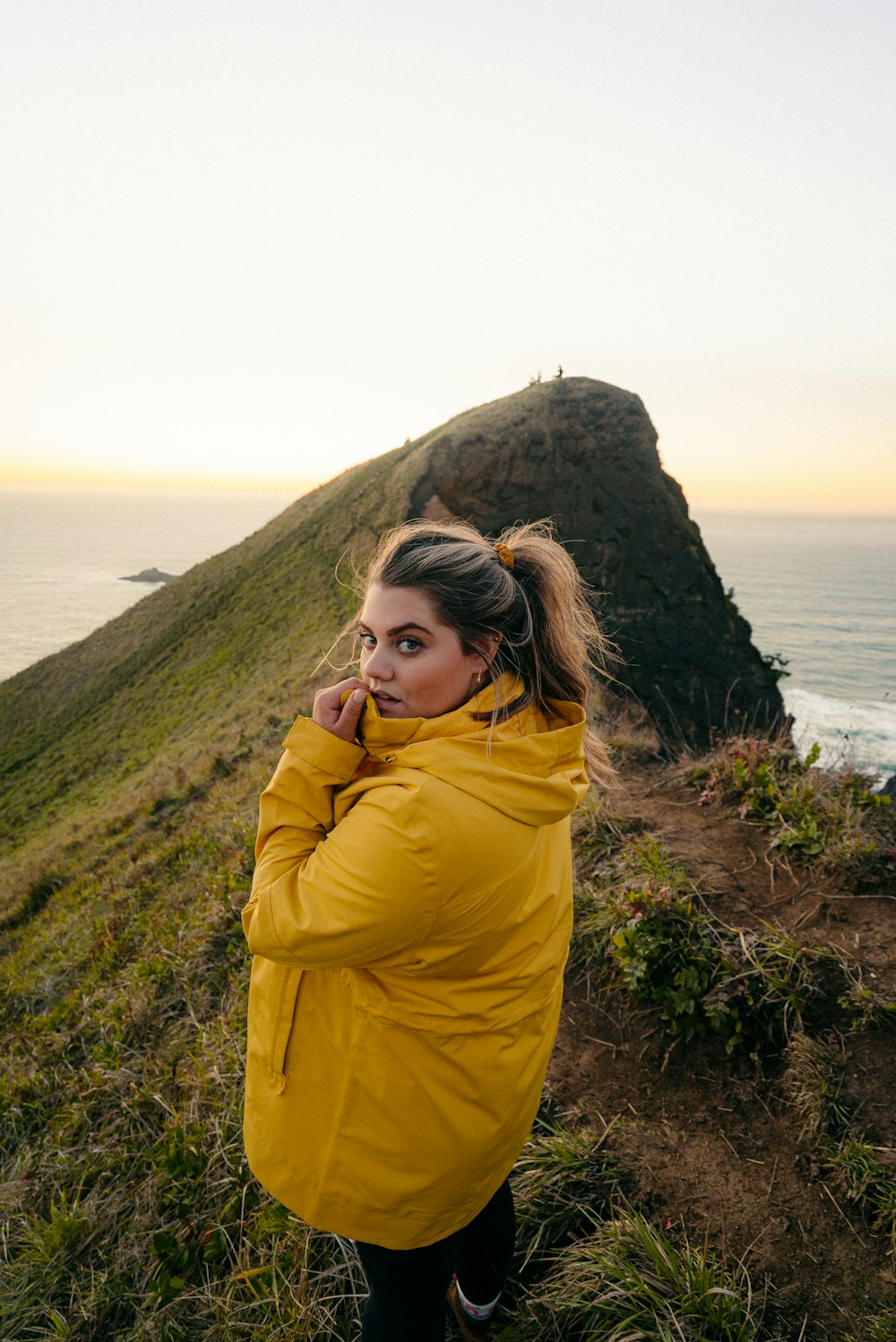 woman in yellow hoodie standing on green grass field near body of water during daytime