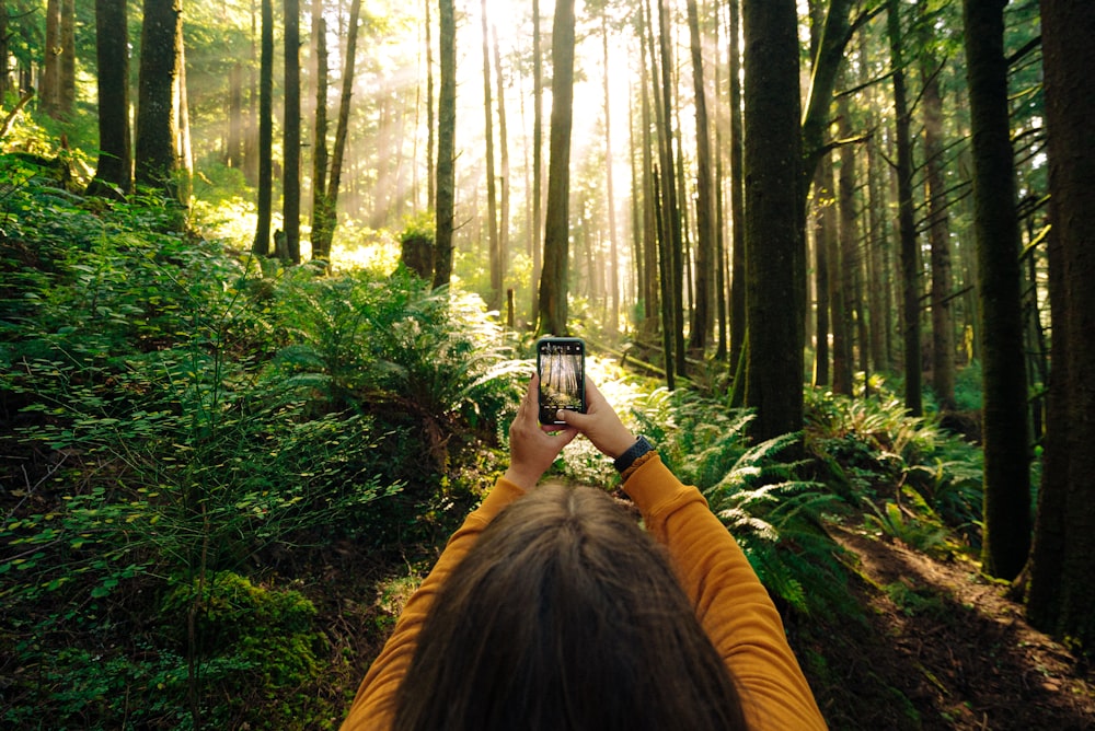 Frau in gelber Jacke fotografiert tagsüber grüne Bäume