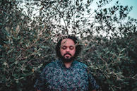 Close-up of a smiling person reflecting with eyes closed, surrounded by nature.