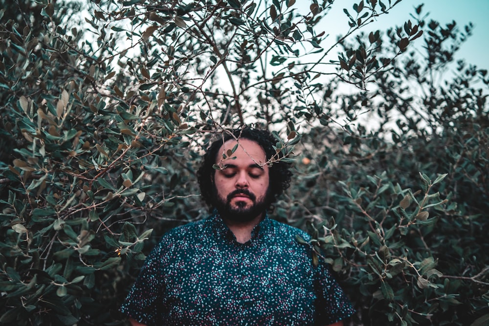 man in blue and white sweater standing behind green plants