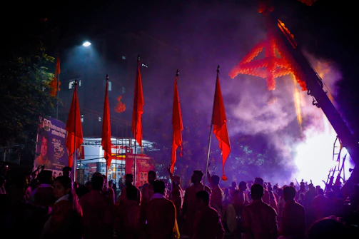 A vibrant crowd at a Kerala political rally waving flags with red and gold hues under dramatic lighting.