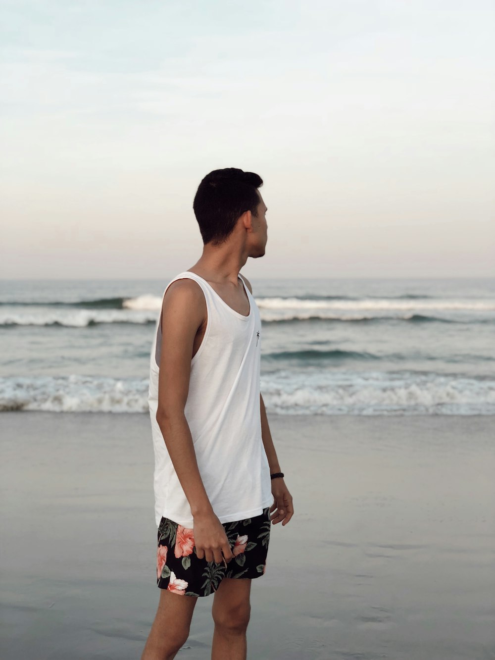 hombre con camiseta blanca sin mangas de pie en la playa durante el día