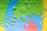 Numerous colorful bubbles of varying sizes are scattered across a multicolored background, creating a vibrant and playful visual effect. The bubbles contain intersecting shades of blue, green, yellow, and red, with some displaying a gradient effect.