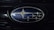 A close-up of an automotive logo featuring several intersecting silver stars on a blue background, surrounded by a chrome oval frame.