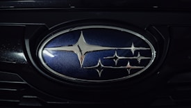 A close-up of an automotive logo featuring several intersecting silver stars on a blue background, surrounded by a chrome oval frame.