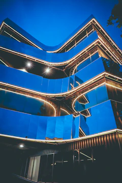 Close-up of a sleek glass building reflecting neon blue lights at dusk.