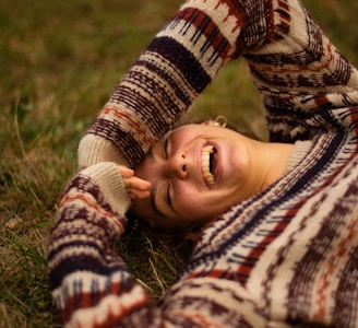 woman in brown and white sweater lying on green grass field during daytime