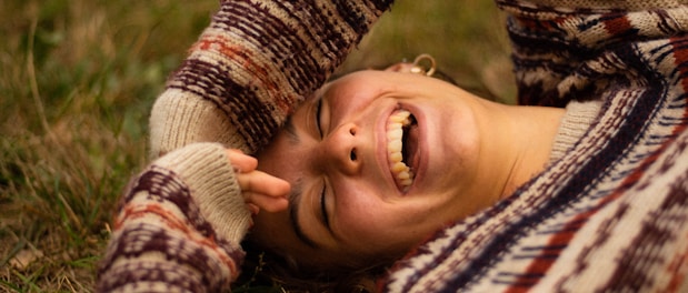 woman in brown and white sweater lying on green grass field during daytime