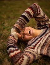 woman in brown and white sweater lying on green grass field during daytime