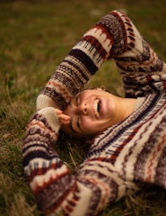 woman in brown and white sweater lying on green grass field during daytime