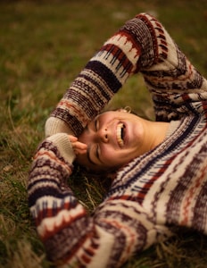 woman in brown and white sweater lying on green grass field during daytime
