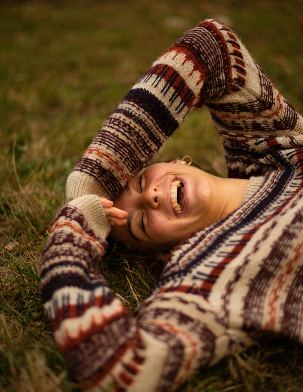 mulher no suéter marrom e branco deitado no campo de grama verde durante o dia