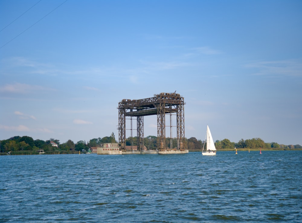 white sail boat on sea near brown concrete bridge under blue sky during daytime