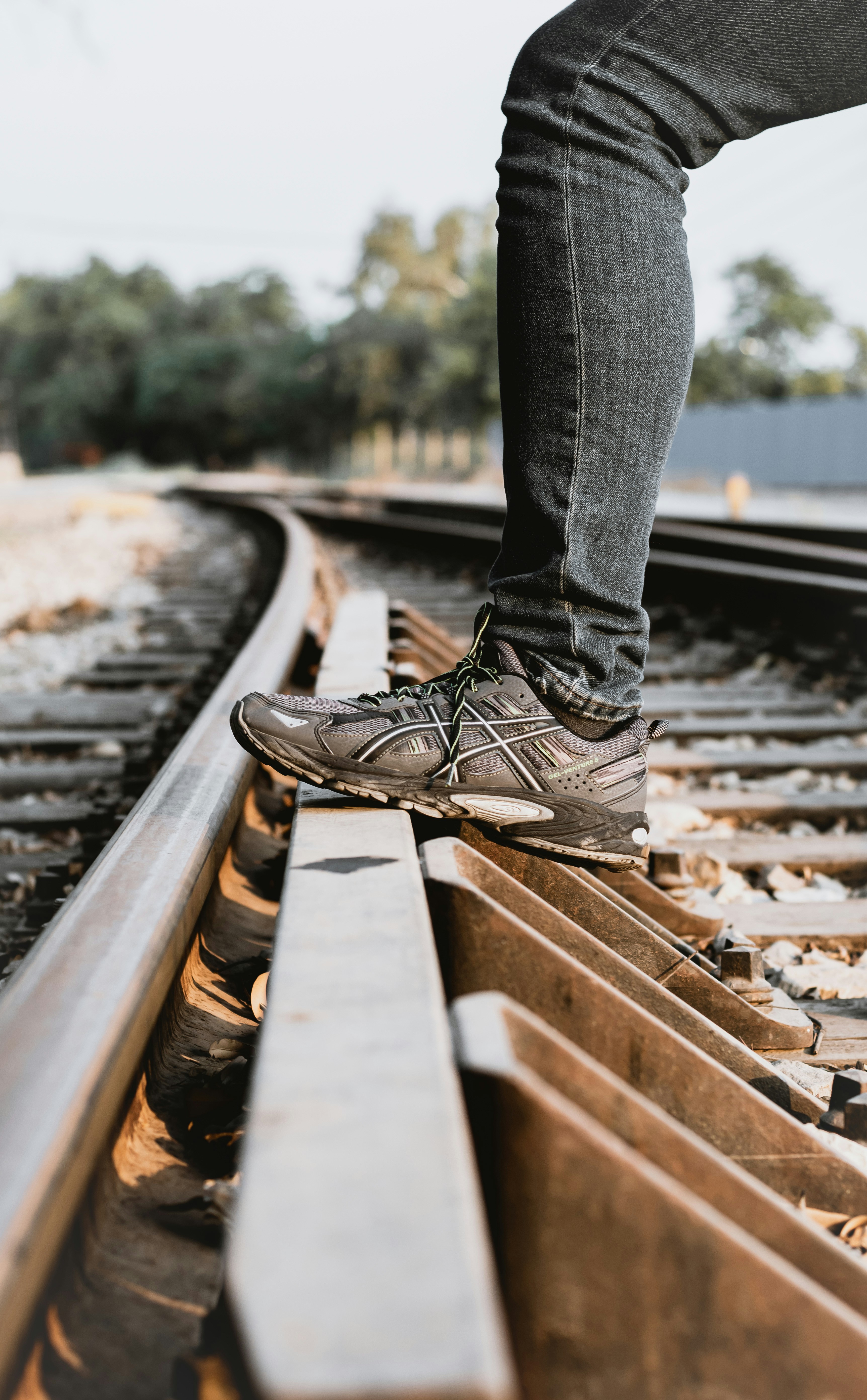personne en jean bleu et chaussures à lacets en cuir noir debout sur le rail de train pendant