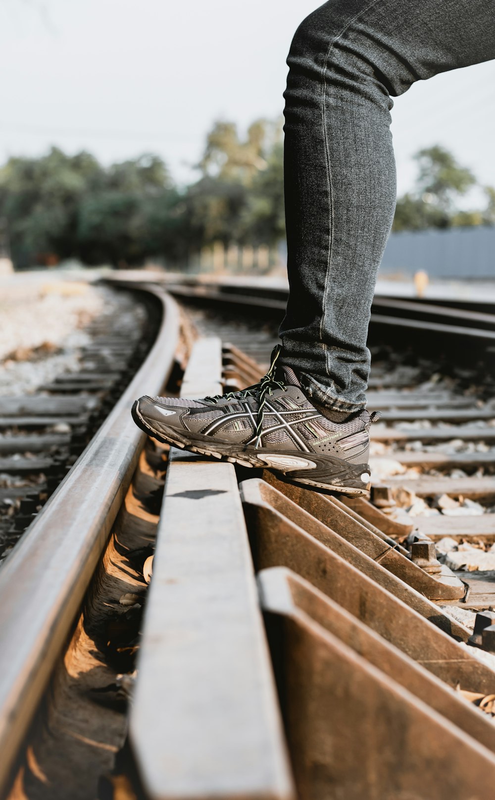 person in blue denim jeans and black leather lace up shoes standing on train rail during