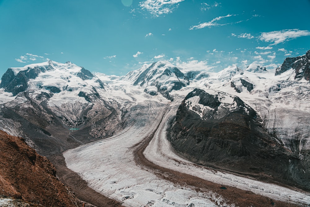 Carretera gris entre montañas cubiertas de nieve bajo el cielo azul durante el día