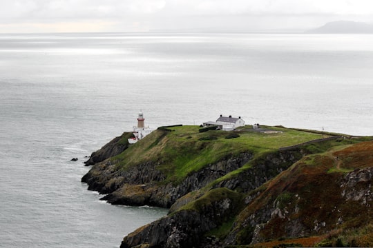 white lighthouse on green grass field near body of water during daytime in Baily Lighthouse Ireland