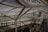 A complex structure composed of curving metal tubes and supports, integrated into a building with large glass windows and an industrial design. The architecture includes staircases, creating a sense of movement and fluidity amid the steel and glass materials.