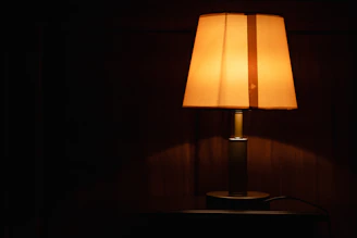 A warm-lit marble base table lamp casting a cozy glow on a rustic wood surface.