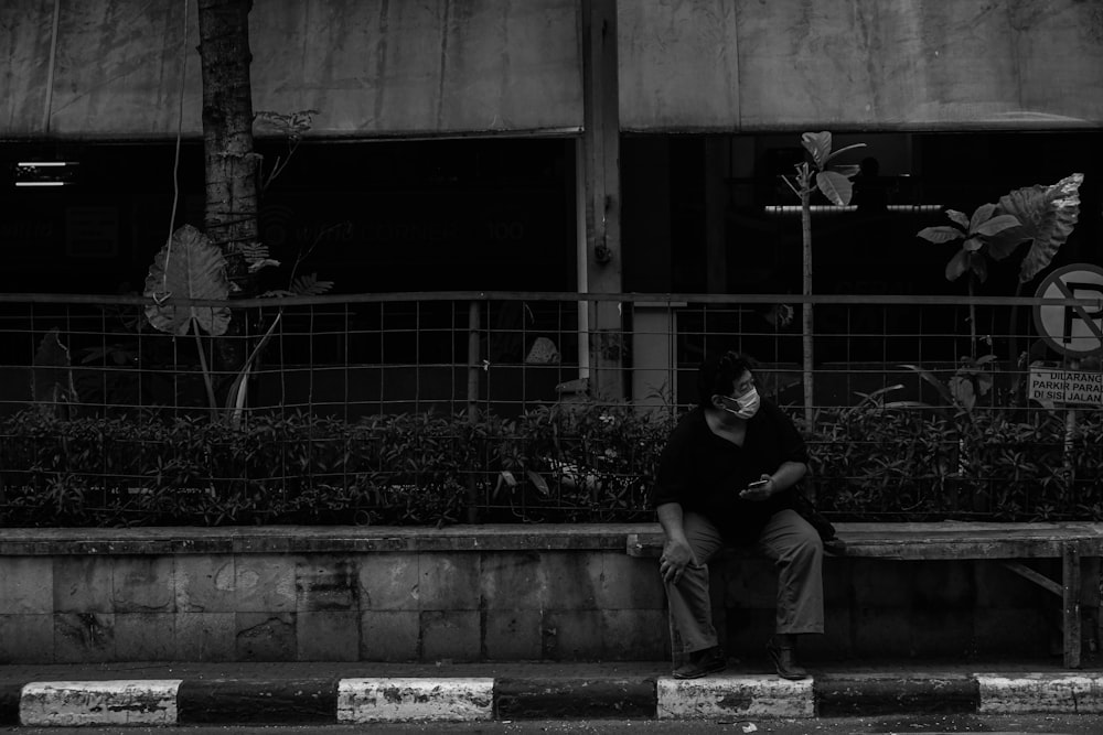 uomo in t-shirt girocollo nera seduto su panchina di cemento